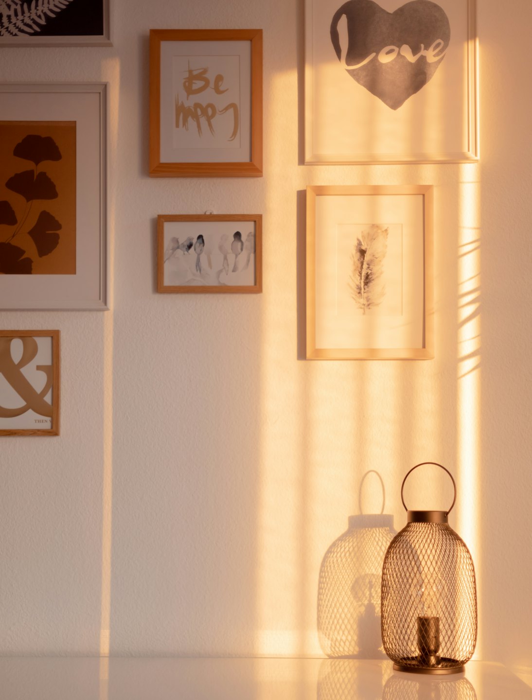 Framed art prints and a glowing lantern sit on a table.