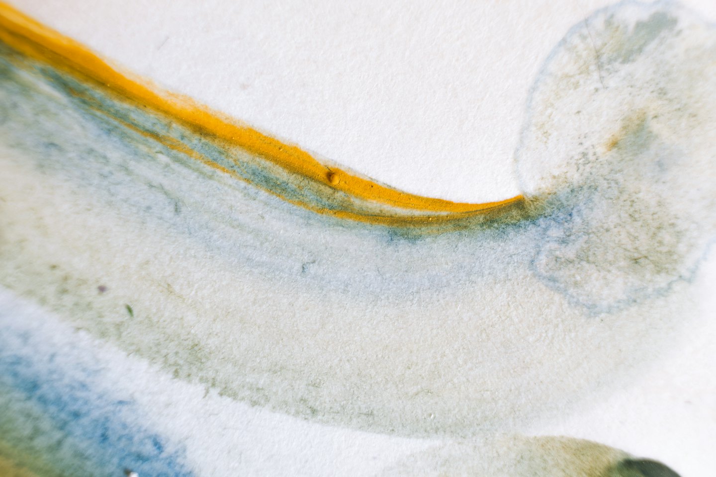 Golden yellow and grey watercolor paints blending on textured paper.